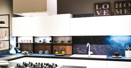 Brightly lit kitchen with black marble counters and backsplash with decorative paintings above kitchen cabinets