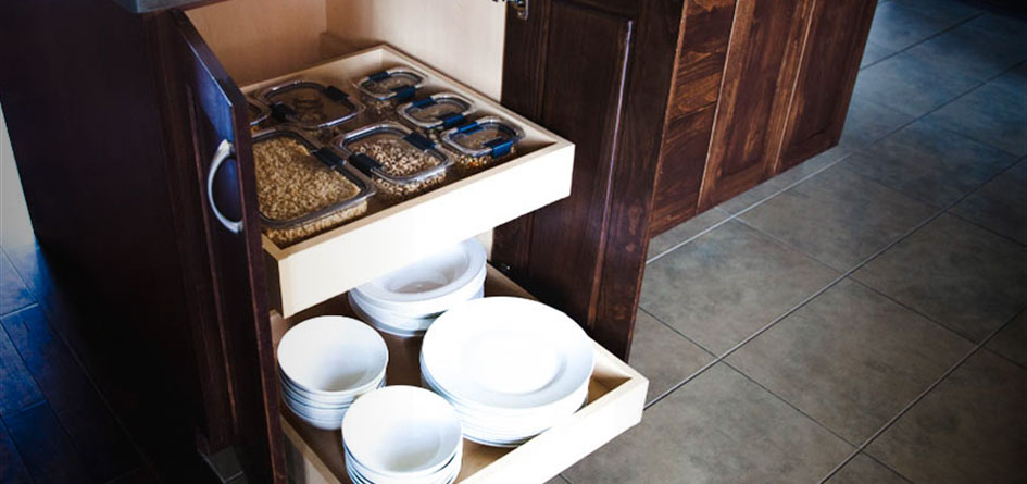 containers with dry goods and white plates on roll out drawers in a brown cabinet.